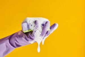 A gloved hand with a soapy sponge