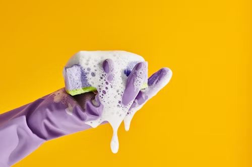 A gloved hand with a soapy sponge
