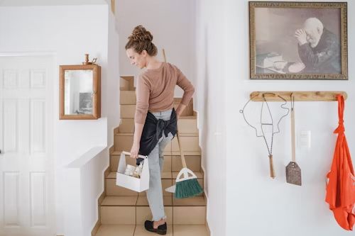 A woman with a broom and other cleaning items, walking up the stairs